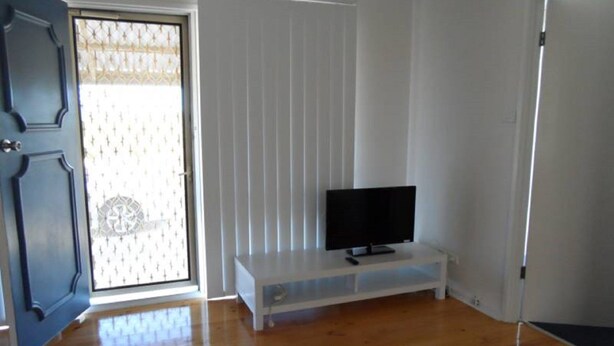 Ein Zimmer mit Holzboden, einer weißen Bank mit Fernseher und einer Tür mit einem ornamentierten Glasfenster.