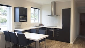A modern kitchen with a dining area, featuring a central island, dark cabinetry, and a stainless steel range hood.