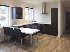 Una cocina moderna con comedor, que incluye una isla central, armarios oscuros y una campana extractora de acero inoxidable.