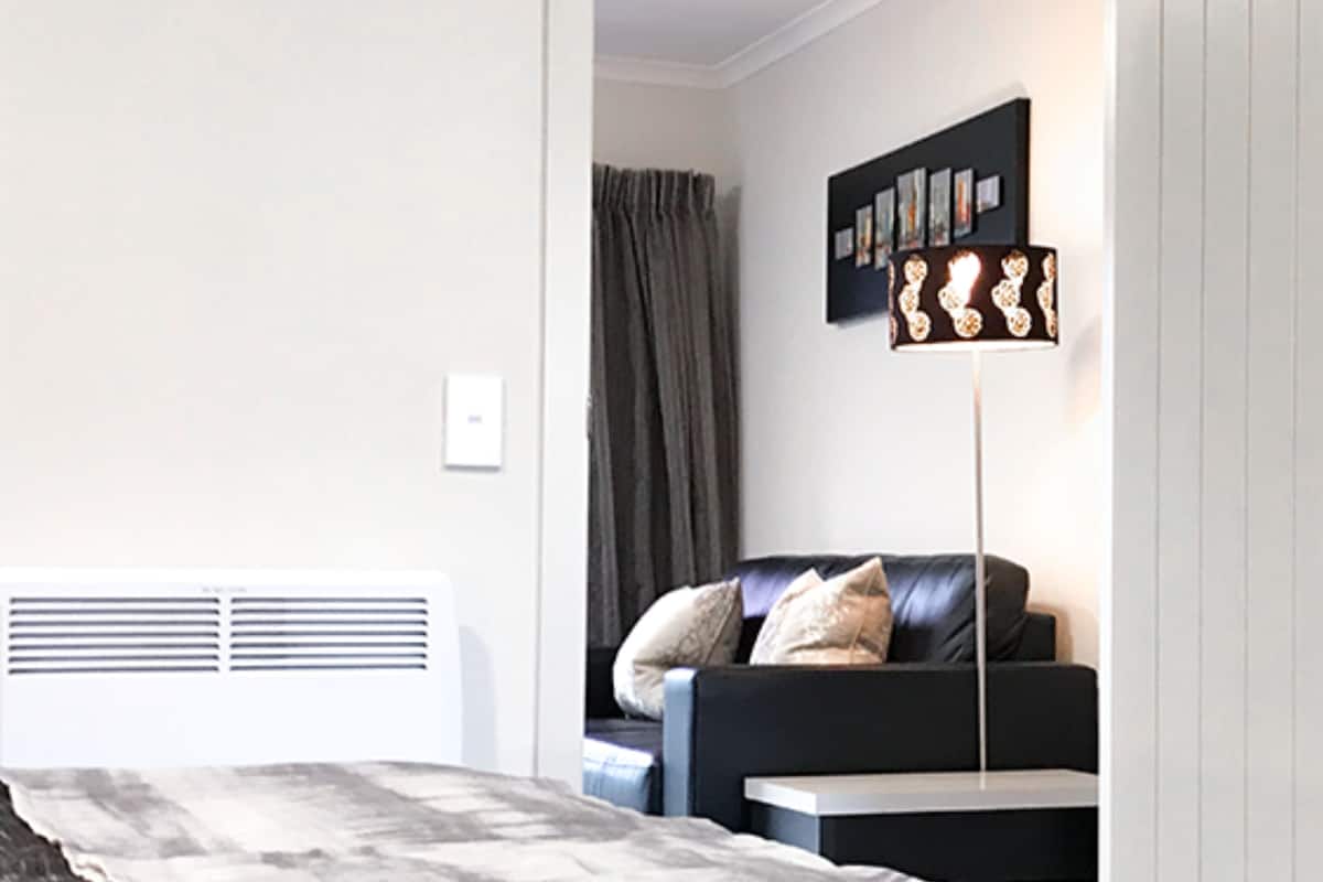 A modern bedroom with a bed, a bedside table, a wall-mounted TV, and a radiator.