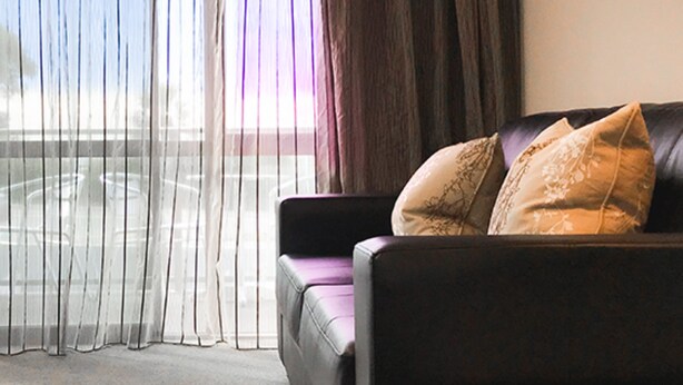 A room with a leather sofa, sheer curtains, and a view of a balcony.