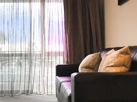 Una habitación con sofá de cuero, cortinas translúcidas y vistas a un balcón.