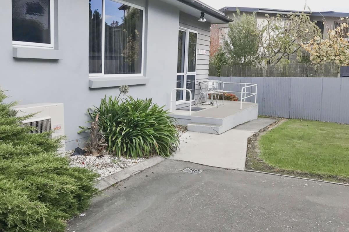 A modern two-story house with a patio, a small garden, and a fenced backyard.