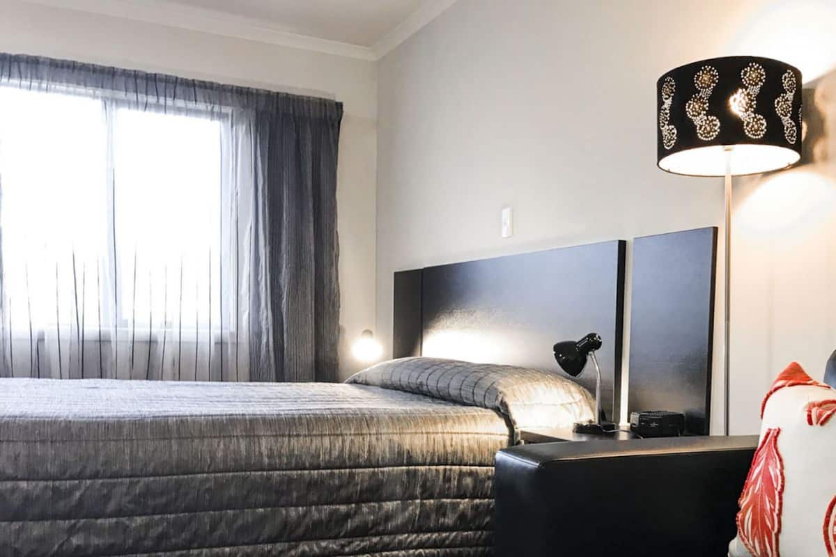 A hotel room with a bed, a desk, a chair, a lamp, and a window with curtains.