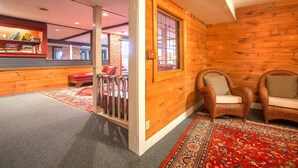 Een gezellige kamer met houten wanden, een rood gekleurd vloerkleed, rieten stoelen en een klein zitgedeelte met een rode bank.