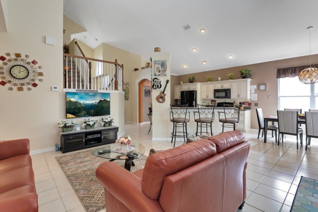 A spacious living area with a leather sofa, a TV, and a dining area with a kitchen in the background.