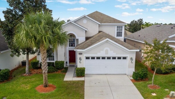 A single-story house with a white garage door, a red door, and a small front yard with a palm tree and shrubs. - 6BR Pool Home Windsor Palms by SHV-2238 (Kissimmee)