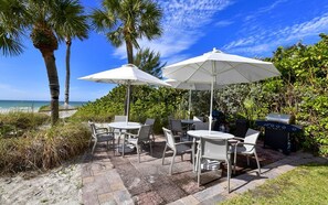 Une terrasse extérieure avec des tables et des chaises, des parasols blancs et un barbecue.