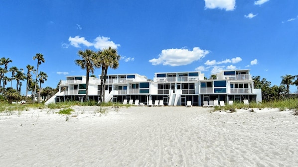 Ein Strandhotel mit mehreren Balkonen, heller Fassade und Palmen.