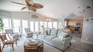 A spacious living room with a large light grey sofa, a round coffee table, and a ceiling fan. - Paw-Paw's Place: Spacious 6BR oceanfront home in Holden Beach, sleeps 14! (Holden Beach)