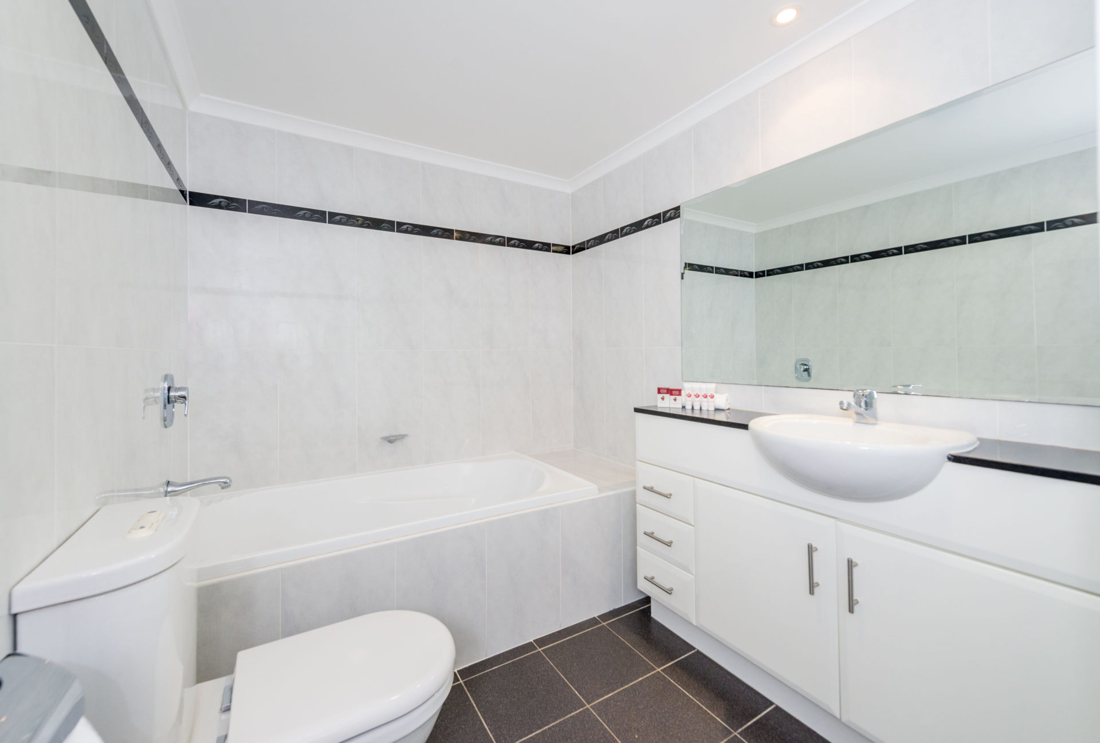 A modern bathroom with a bathtub, toilet, sink, and vanity with a mirror.