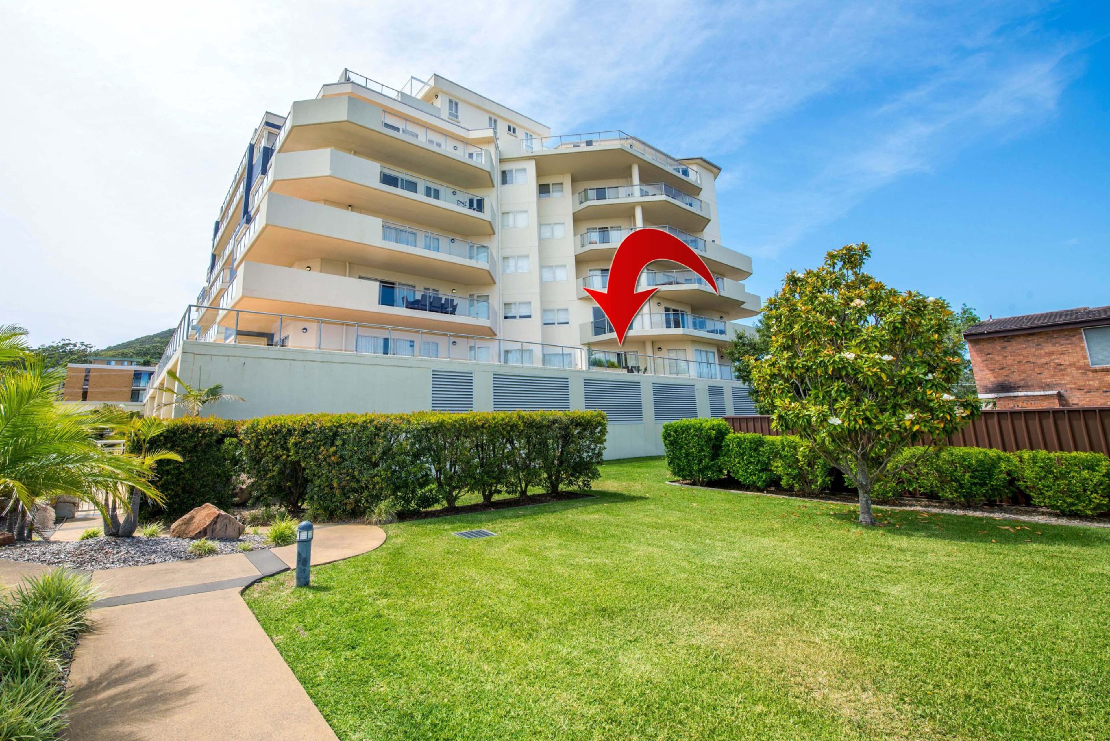 A multi-story residential building with balconies, a well-maintained lawn, and a clear sky.