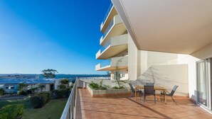 Varanda com vista para o mar, mesa com cadeiras e um pequeno jardim.