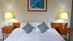 Quarto de hotel com uma cama grande, duas mesas de cabeceira com luminárias, um quadro emoldurado na parede e uma cabeceira de madeira.