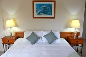 Een hotelkamer met een groot bed, twee nachtkastjes met lampen, een ingelijste foto aan de muur, en een houten hoofdbord.