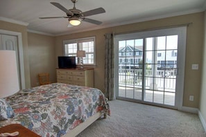 A bedroom with a bed, a television, a dresser, and a sliding glass door leading to a balcony.