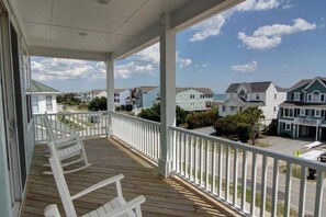 Eine überdachte Veranda mit weißen Geländern, einer Holzterrasse und Blick auf angrenzende Häuser.