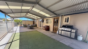 A covered patio area with a barbecue grill, seating, and a small lawn.
