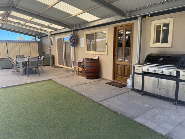 Un espace extérieur aménagé en patio, avec un barbecue, une table et des chaises, ainsi qu’une petite pelouse.