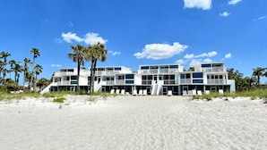 Ein Strandhotel mit mehreren Balkonen und einem Sandstrand im Vordergrund.