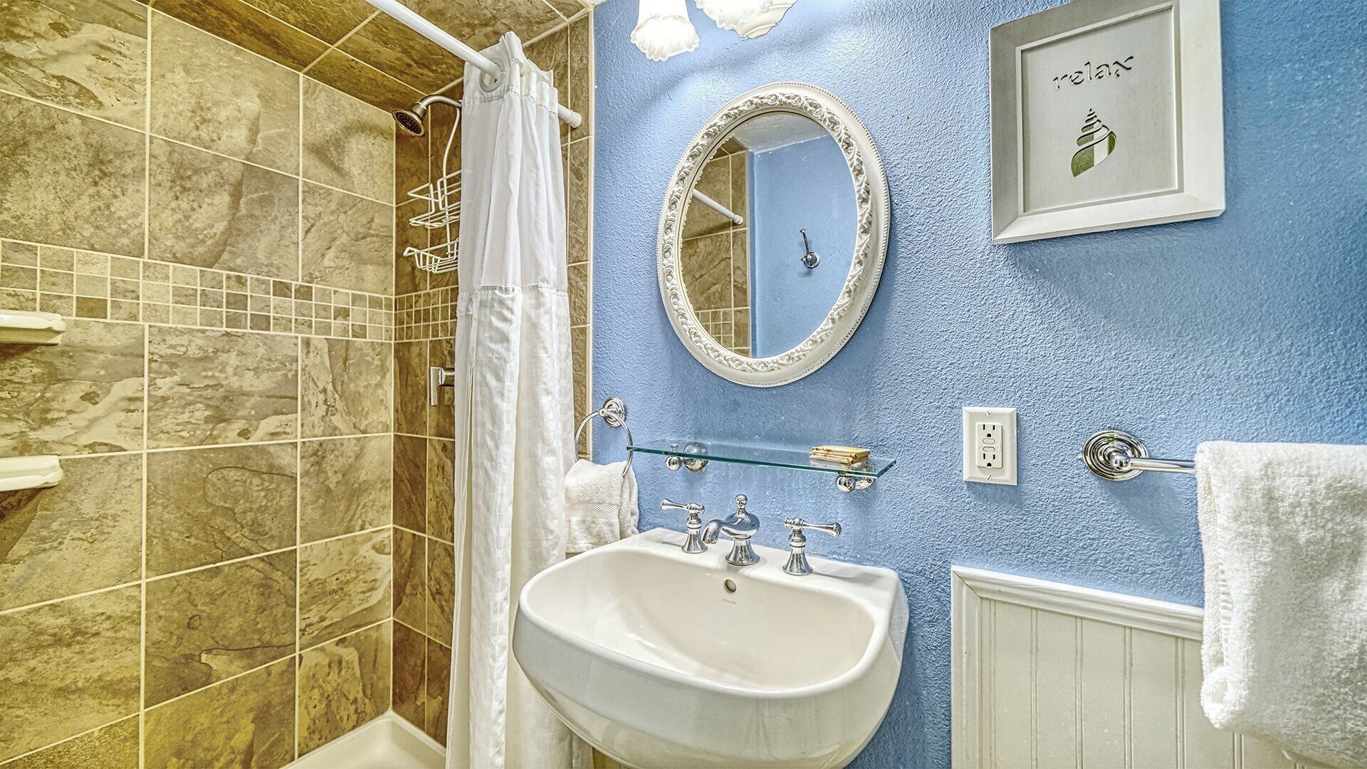 A bathroom with a shower, a sink, a mirror, and a towel rack.