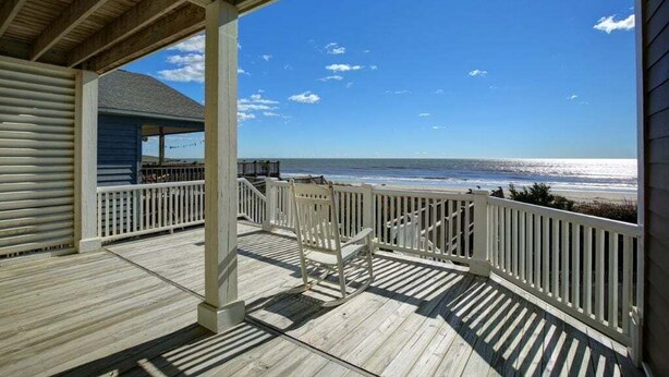 Una terraza de madera con barandilla, zona cubierta y vista a la playa.