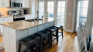 Una cocina moderna con armarios blancos, electrodomésticos de acero inoxidable, una encimera de granito y una isla grande con taburetes de bar.