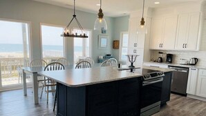 A modern kitchen with a large island, white cabinets, and a view to the outside. - Oceanfront bliss awaits at Our Sand Dune, a spacious 5-bedroom retreat in Holden Beach. (Holden Beach)