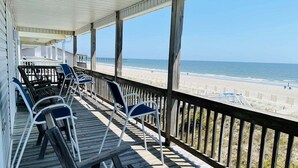 A covered outdoor area with wooden deck, chairs, and a view of the beach. - Oceanfront bliss awaits at Our Sand Dune, a spacious 5-bedroom retreat in Holden Beach. (Holden Beach)