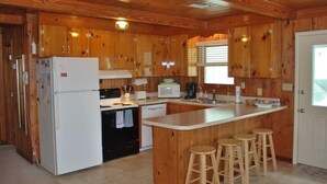Una cocina de estilo cabaña de madera con refrigerador, estufa, microondas y taburetes de bar.