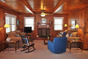 A cozy living room with wooden walls, a fireplace, a television, and two couches.