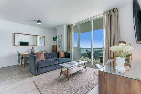 A modern living room with a grey sofa, a coffee table, and a dining area with a table and chairs.