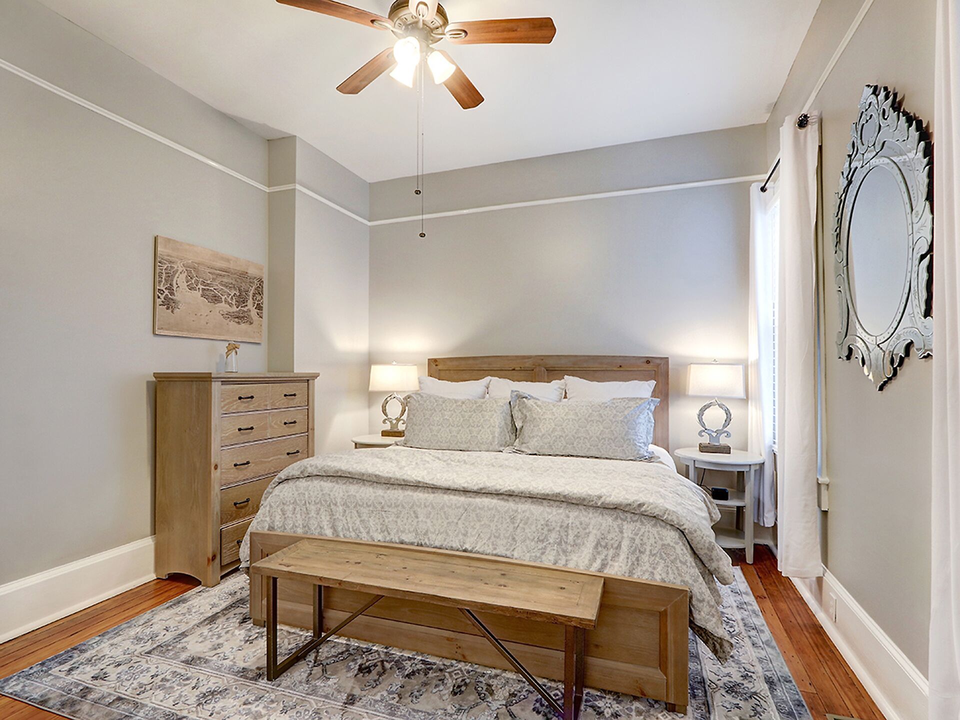 A bedroom with a wooden bed, bedside lamps, a ceiling fan, a wooden dresser, and a patterned rug.