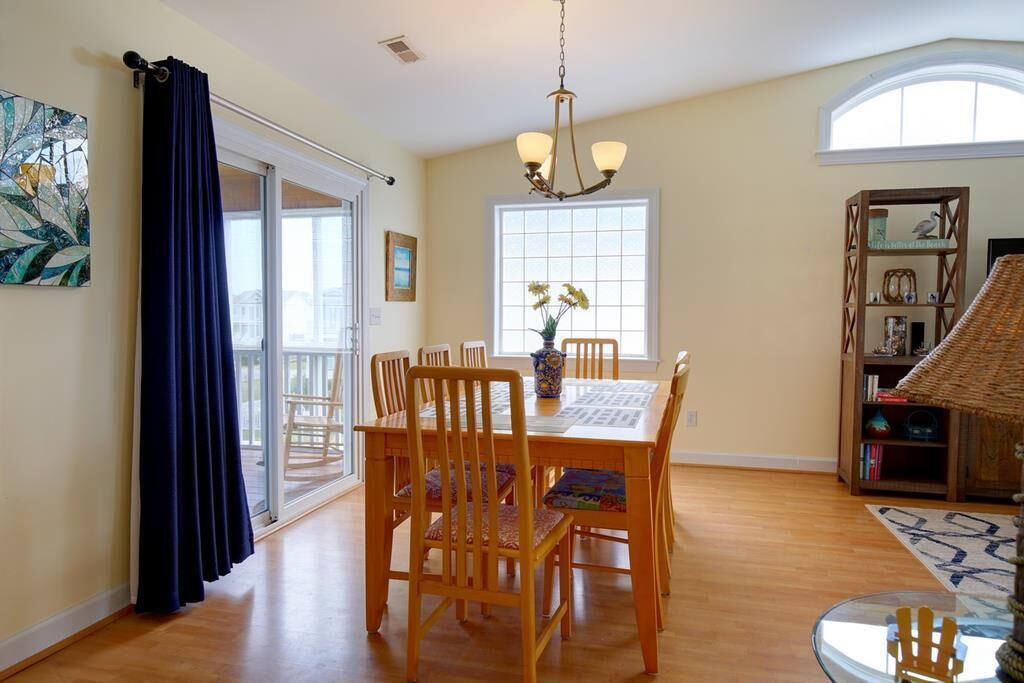 A dining area with a wooden table and chairs, a chandelier, and a bookshelf with decorative items.