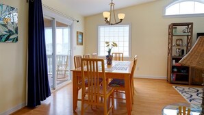 A dining area with a wooden table and chairs, a chandelier, and a bookshelf with decorative items. - Casa de la Playa: Spacious 4BR home in Holden Beach, perfect for family getaways. (Holden Beach)