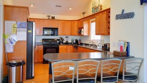 A modern kitchen with wooden cabinets, stainless steel appliances, and a central island with bar stools. - Casa de la Playa: Spacious 4BR home in Holden Beach, perfect for family getaways. (Holden Beach)