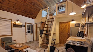 A cozy cabin interior with a dining area, kitchen, and a loft bedroom with a wooden staircase.