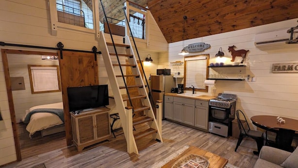 A cozy cabin-style interior with a loft bedroom, a kitchen with a stove, and a dining area.