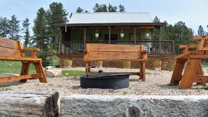 A rustic cabin with a wooden deck, outdoor seating, and a metal roof.