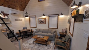 A cozy living room with a sofa, coffee table, and chairs, a staircase, and a kitchen area with a stove and sink.