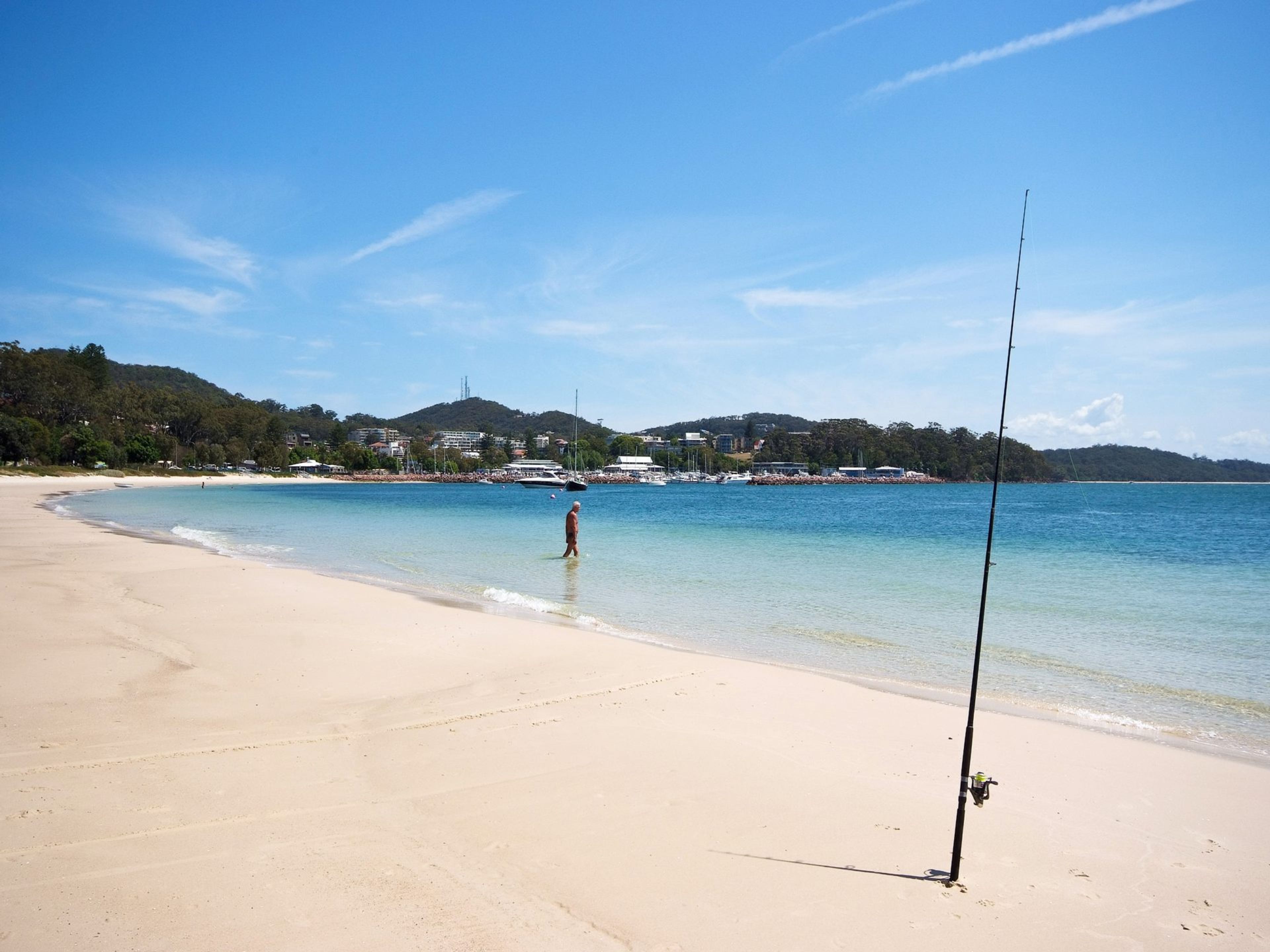 Ein Strand mit einer Angel, klarem Wasser und einer hügeligen Landschaft mit Gebäuden im Hintergrund.