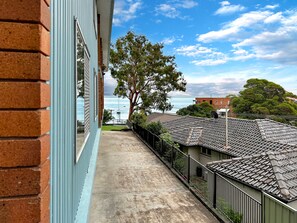 Un balcone con vista sul mare, un albero e un edificio con tetto in tegole.