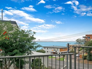 A residential area with a clear view of the sea, a street with parked cars, and a balcony overlooking the street.