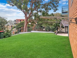 A well-maintained backyard with a lawn, a large tree, and a wooden fence.
