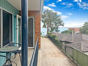Een balkon met uitzicht op zee, een tafel met stoelen en een deur voorzien van een muggengaas.