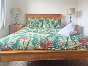 A bed with a tropical leaf pattern bedspread, wooden headboard, two bedside lamps, and a white towel on the bed.