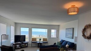 Ett vardagsrum med tv, sittmöbler, ett bord och utsikt över havet.