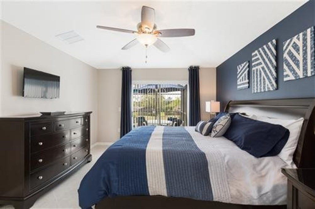 A bedroom with a bed, a dresser, a ceiling fan, and artwork on the wall.