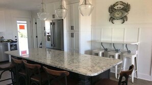 Una cocina con una isla grande, taburetes de bar, lámparas colgantes y un reloj en la pared.