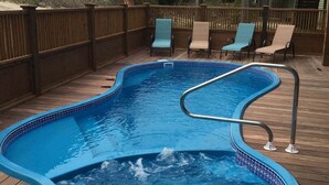 Una piscina con muelle de madera, sillas de descanso y una cerca también de madera.